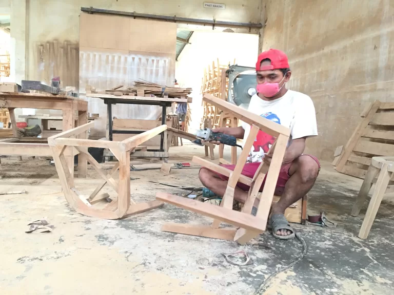 Worker working a wooden part with a hand-held power tool at the part-making area